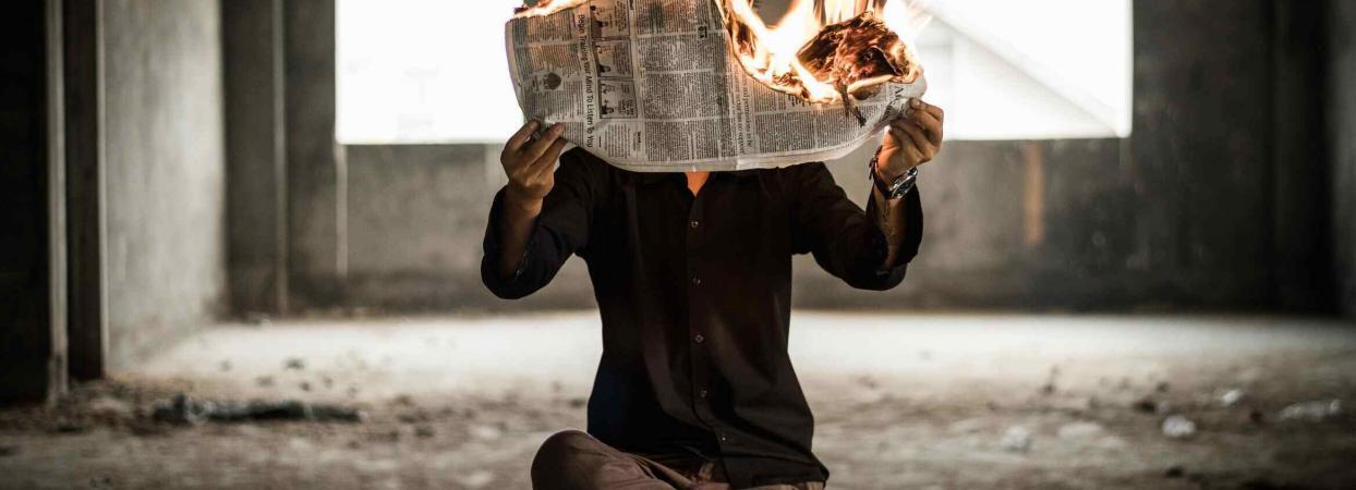 man sites in chair while burning a newspaper